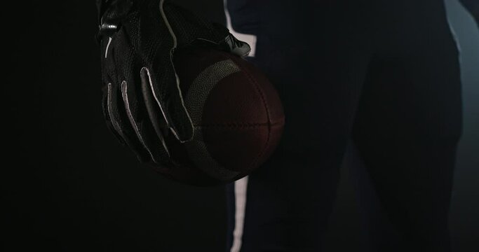 American football sportsman player holding a ball on black background close up