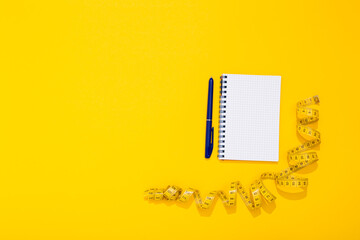 Twisted centimeter tape and spiral note book and pen with copy space on yellow background. Greeting postcard. Body measurement. Nutrition and fitness workout plan. International Women Day 8 March