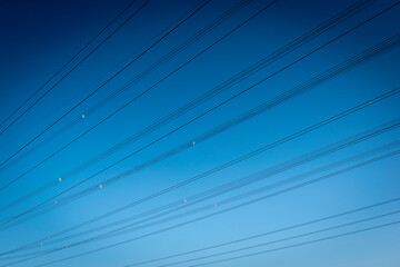 Hochspannungskabeleiner Stromtrasse ziehen diagonal durch das Bild mit blauem Himmel im Hintergrund
