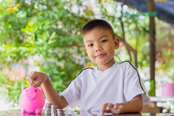 Portrait of happy Asian child boy putting coins in to the pink pig can. Childhood insert money in the bottle. Kid saving money for the future concept. Children learning.