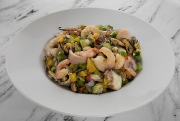 Colorful salad. Seafood ad vegetables. Top view of a mediterranean flavor salad with sliced squid, mussels, shrimps, onion, avocado, mango and bell peppers, served on a white deep plate on the table.