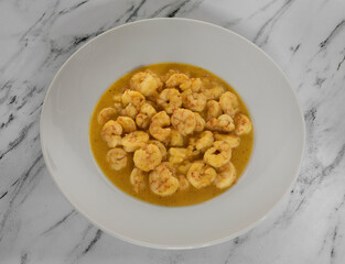 Gastronomy. Seafood. Closeup view from above of cooked shrimps with a mustard and honey sauce, presented on a white deep plate on the marble table.