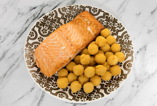 Gourmet gastronomy. View from above of a delicious baked salmon filet with a fried noisette potatoes garnish, served on a decorative deep plate on the marble table.