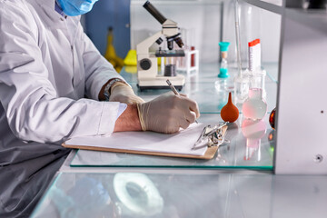 cropped male scientist make notes while analyzing the test tubes in lab, writing on paper,in medical wear, doing research and experiment about genetic to find drugs to treat covid-19