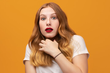 Portrait of the scared girl with wavy redhead, wearing white t-shirt, isolated on yellow background