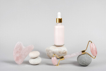 Obraz na płótnie Canvas Crystal rose quartz facial roller, massage tool Gua sha and anti-aging collagen, serum in glass bottle on stones, grey background. Facial massage for natural lifting, Beauty concept