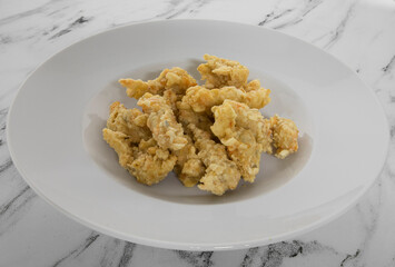Gourmet cuisine. Fried seafood. Closeup view of breaded deep fried crab fingers presented on an elegant white deep plate on the marble table. 