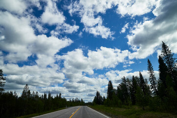 View from relief car windscreen on the blue sky with white clouds, grey asphalt road and landscape with forest and green teeses. Landscape through window