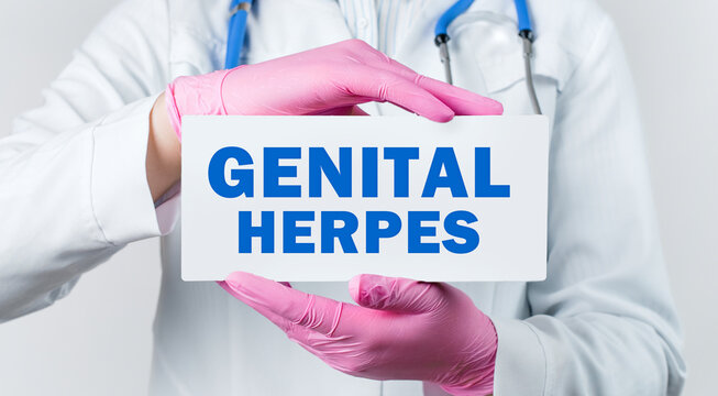 Cropped view of female doctor in a white coat and pink sterile gloves holding a card with words - GENITAL HERPES