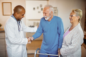 Happy black doctor greeting senior couple at nursing home.