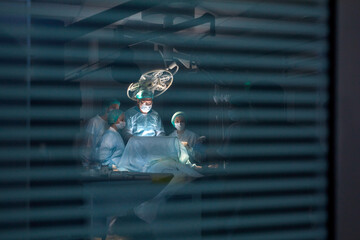 Fototapeta na wymiar shot of technologically advanced operating room with doctors making operation to patient, photo through the glass. real Modern Operating Theater With Working equipment