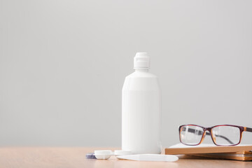 Container with contact lenses, solution, eyeglasses and tweezers on table