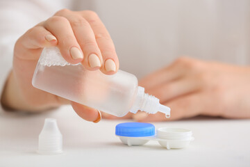Woman pouring solution in container with contact lenses, closeup