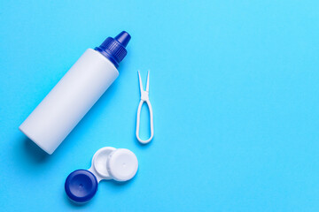 Container with contact lenses, solution and tweezers on color background