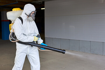 disinfector in hazmat suit working with pressure washer or sanitizer outdoors, wearing medical mask, gloves and goggles