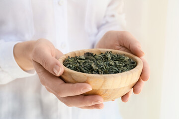 Woman with dry tea leaves in bowl, closeup