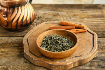 Bowl with dry green tea and cinnamon on wooden table