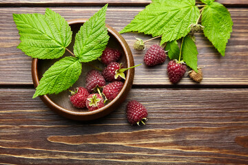 Fototapeta na wymiar Fresh raspberry red berries with green leaves in bowl on wooden table