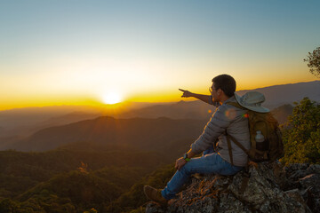 Fototapeta na wymiar Young man hiker on a top of a mountain standing on top of cliff in summer mountains at sunset and enjoying view of nature