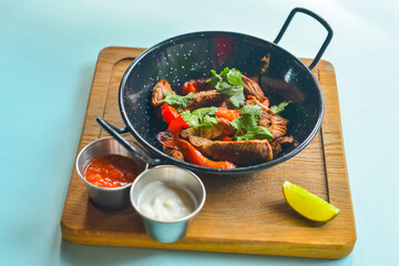 Vegetables and meat in wok pan served with lavash bread and different kinds of sauce. Over pastel blue background.