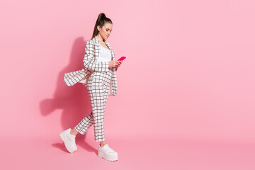 Photo portrait full body view of woman walking texting holding phone in two hands isolated on pastel pink colored background