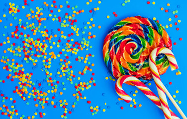 Christmas composition. Large lollipop, red and white striped candies and multicolor round candies on a blue background. Flat lay, copy space, top view.