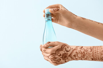 Beautiful female hands with henna tattoo and bottle on light background