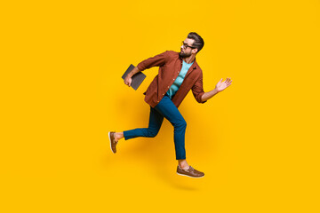 Full length body size photo of confident entrepreneur running with laptop looking back isolated on bright yellow color background