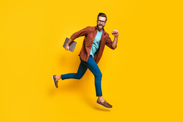Fototapeta na wymiar Full length body size photo of man running fast keeping laptop freelancer smiling isolated on bright yellow color background