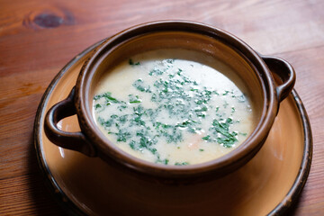 Soup with herbs in a clay plate close-up.