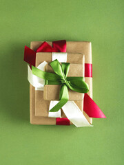 Three beautifully packed presents with the multicolor satin ribbons and craft paper on the green background.
