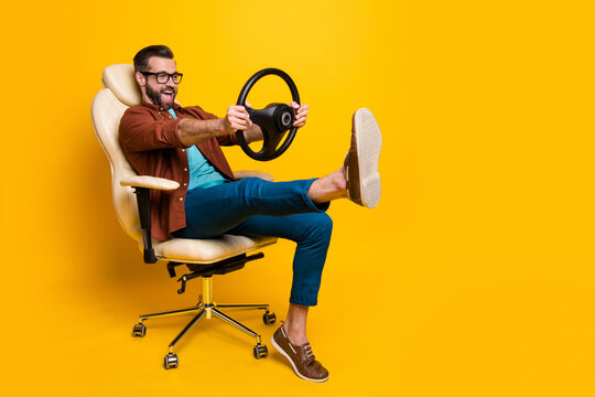Full length body photo of happy fooling man in chair keeping steering wheel pretending car driver isolated vivid yellow color background