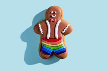 Gay Christmas bakery. Lgbt pastry. Sexual identity. Homemade cookies. Chocolate icing gingerbread man rainbow shorts isolated on blue pastel background.