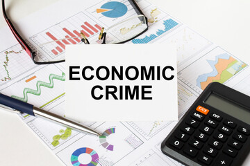 White card with text Economic Crime it is lies on financial charts with a calculator and eyeglasses