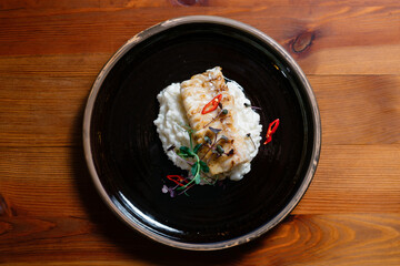 Fish fillet baked with rice on a black plate.