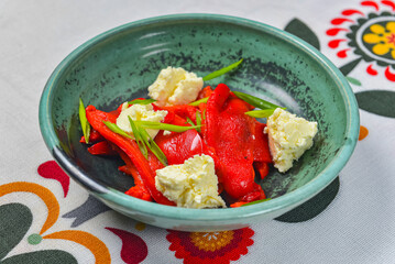 Baked pepper Salad with feta cheese, vegetable salad served in a bowl over traditional Ukrainian tablecloth.