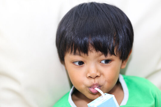 An Asian Young Boy Holding And Drinking A Carton Of Milk.