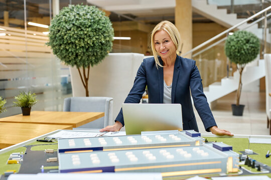 leading architect woman work on laptop while planning process of building, uses small 3d model scale of future building in the office