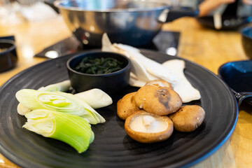 Assorted vegetables and mushrooms on a black plate for hot pot.