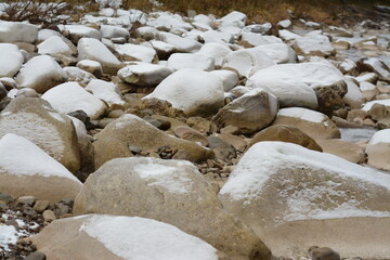 Large stone cobblestones covered with snow on the bank of a mountain river
