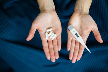 The girl is holding an electronic thermometer and pills for the treatment of the new COVID-19 virus.