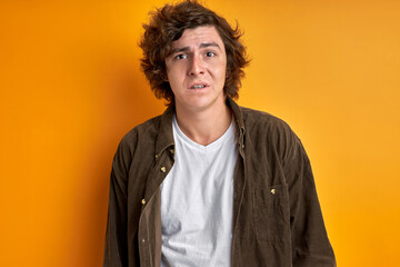 man at a loss, look at camera, male is confused and unhappy isolated on orange background