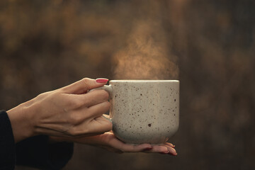 A Cup of hot tea with steam in a woman's hands