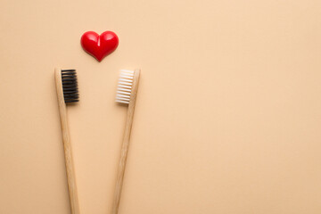 Valentines day concept. Top above close up view photo of two bamboo eco-friendly wooden toothbrushes with black and white bristle and red heart isolated beige background with empty blank space