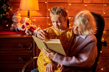 elderly woman love spending time with her cute granddaughter in decorated room, they look at book...