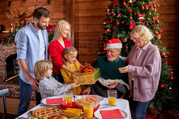 excited family congratulating each other with chrstmas or new year, sharing gifts, present. they sit behind decorated table and enjoy