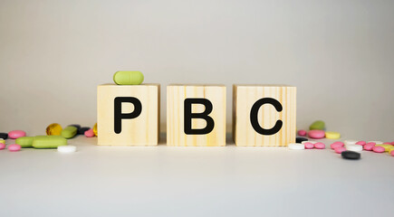 PBC Primary biliary cholangitis - word from wooden blocks with letters on white background surrounded with colorful pills.Medical concept.