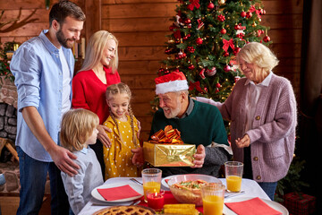 excited family congratulating each other with chrstmas or new year, sharing gifts, present. they sit behind decorated table and enjoy