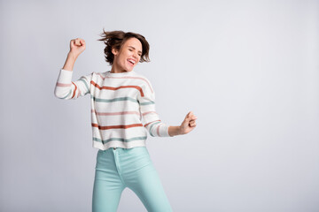 Photo of funny charming young woman dressed striped pullover dancing rising fists empty space...