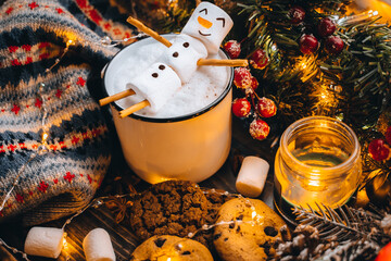 Christmas food white cup with hot chocolate snowman marshmallows. homemade cookie, cinnamon sticks fir xmas tree branches with warm garland lights. New year celebration. Festive dessert breakfast idea